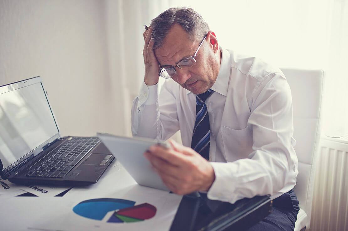 Hard working Mature Adult man working in the office, on a digital tablet, looking concerned